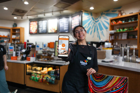 Woman holding a mobile phone with the Klatch Coffee app