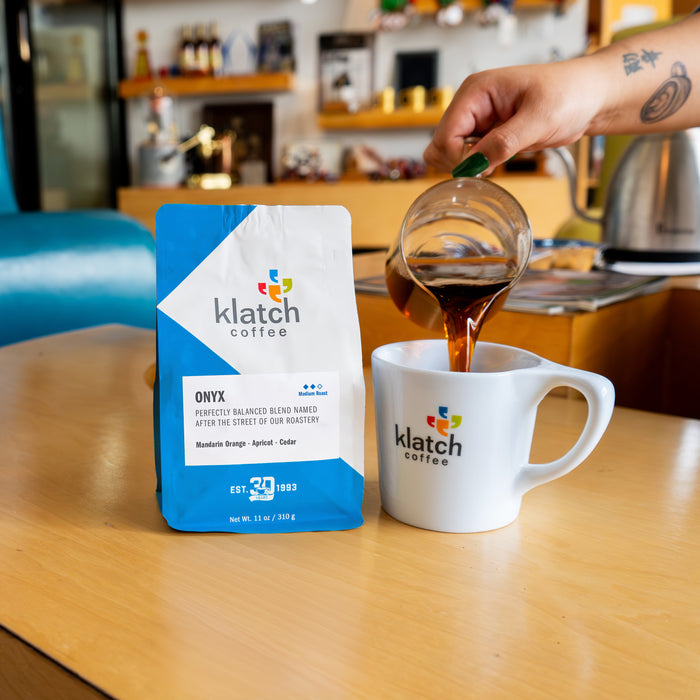 Hand pour coffee into a Klatch coffee mug adjacent to a bag of onyx coffee.